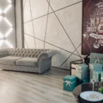 Modern living room with a grey tufted sofa, geometric wall design, LED light accents, and Christmas decorations including gift boxes and a festive “Merry Holly Jolly Christmas” poster.