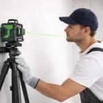 Worker using a laser level on a tripod to project a green horizontal line on a wall for accurate wall leveling before tiling.