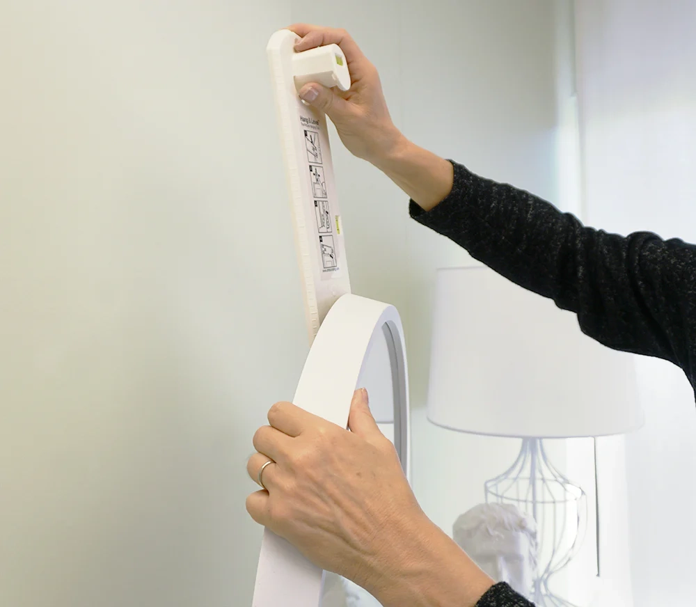 Applying strong adhesive strips to the back of a mirror for secure, damage-free wall mounting without nails.