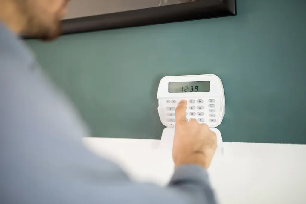 Alt text: A person pressing buttons on a wall-mounted home security keypad displaying the time 12:39. 