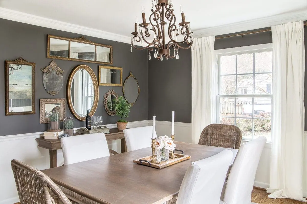 An eclectic collection of vintage-style mirrors in varied shapes and ornate gold frames creates a sophisticated, light-reflecting focal point against the moody charcoal gallery wall.