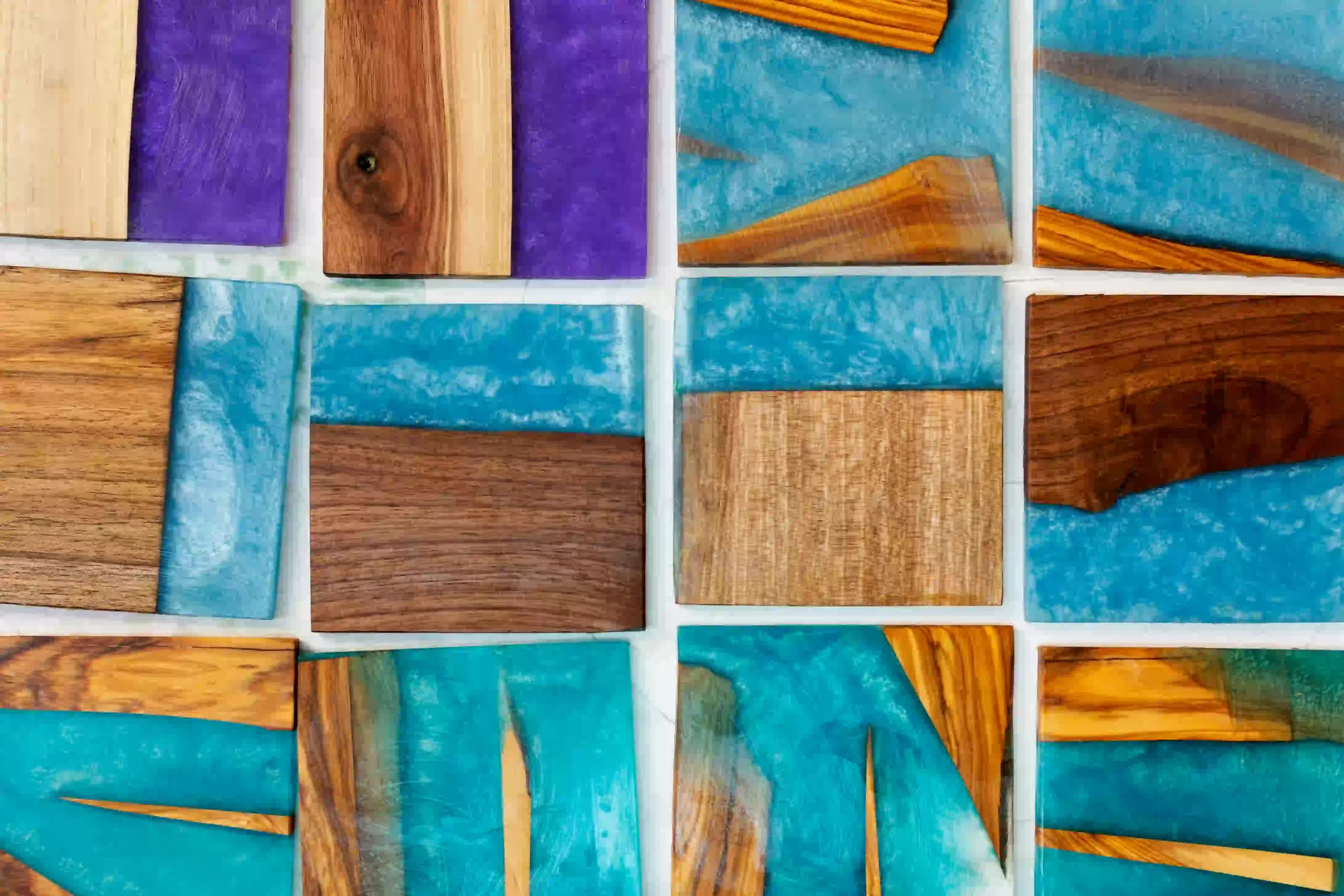 Close-up of colorful wooden and resin tile pieces arranged in a grid pattern, featuring natural wood grains mixed with blue and purple epoxy designs.