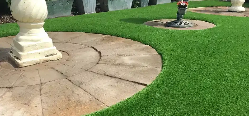 Artificial grass installed around a circular stone patio with decorative planters and garden features, demonstrating a clean, low-maintenance landscaping design.