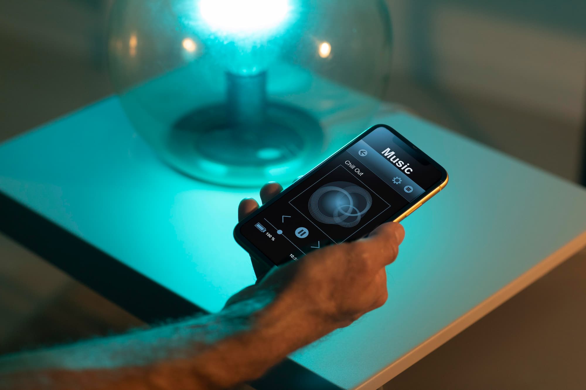 Hand holding smartphone controlling music beside glowing lamp