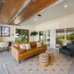modern living room with light grey flooring, leather sofa, wooden ceiling and large windows opening to garden