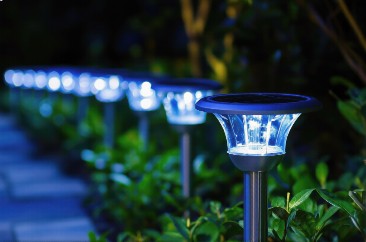 Modern stainless steel garden solar lights with cool blue LED illumination lining a backyard stone pathway at night, featuring integrated solar panels for eco-friendly outdoor landscape lighting.