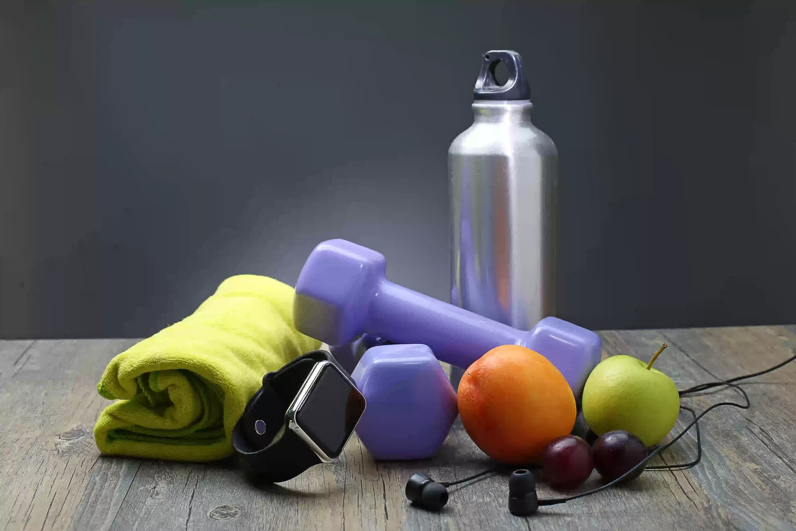 A clean and inspiring home gym setup featuring essential DIY fitness accessories arranged neatly in a cozy corner of a room. The space includes a pair of dumbbells resting on a rubber mat, a rolled-up yoga mat leaning against the wall, and colorful resistance bands hanging from a simple wall hook