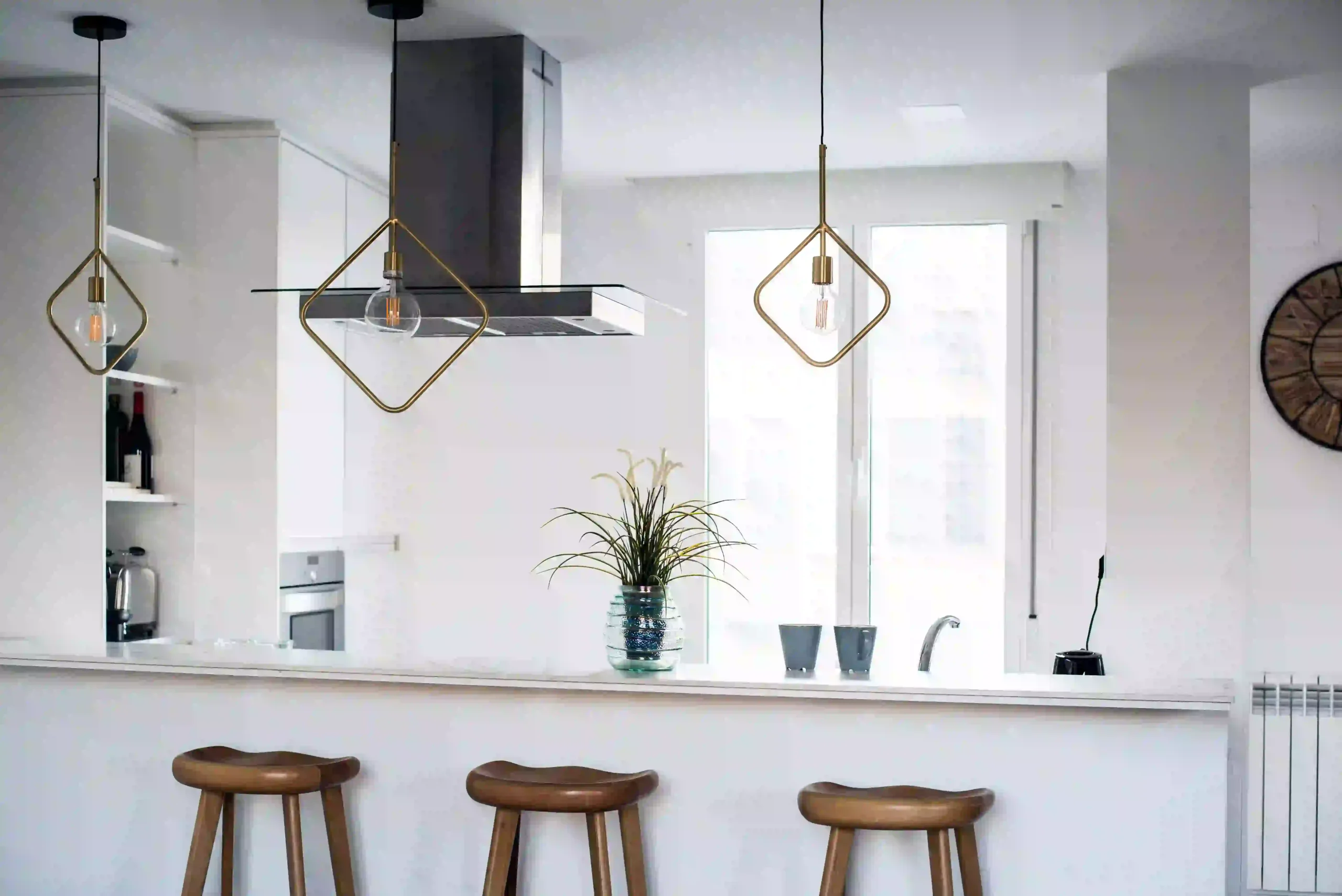 Modern white kitchen interior design with stylish pendant lights, sleek cabinets, marble countertops, wooden accents, and a spacious house layout with natural lighting.